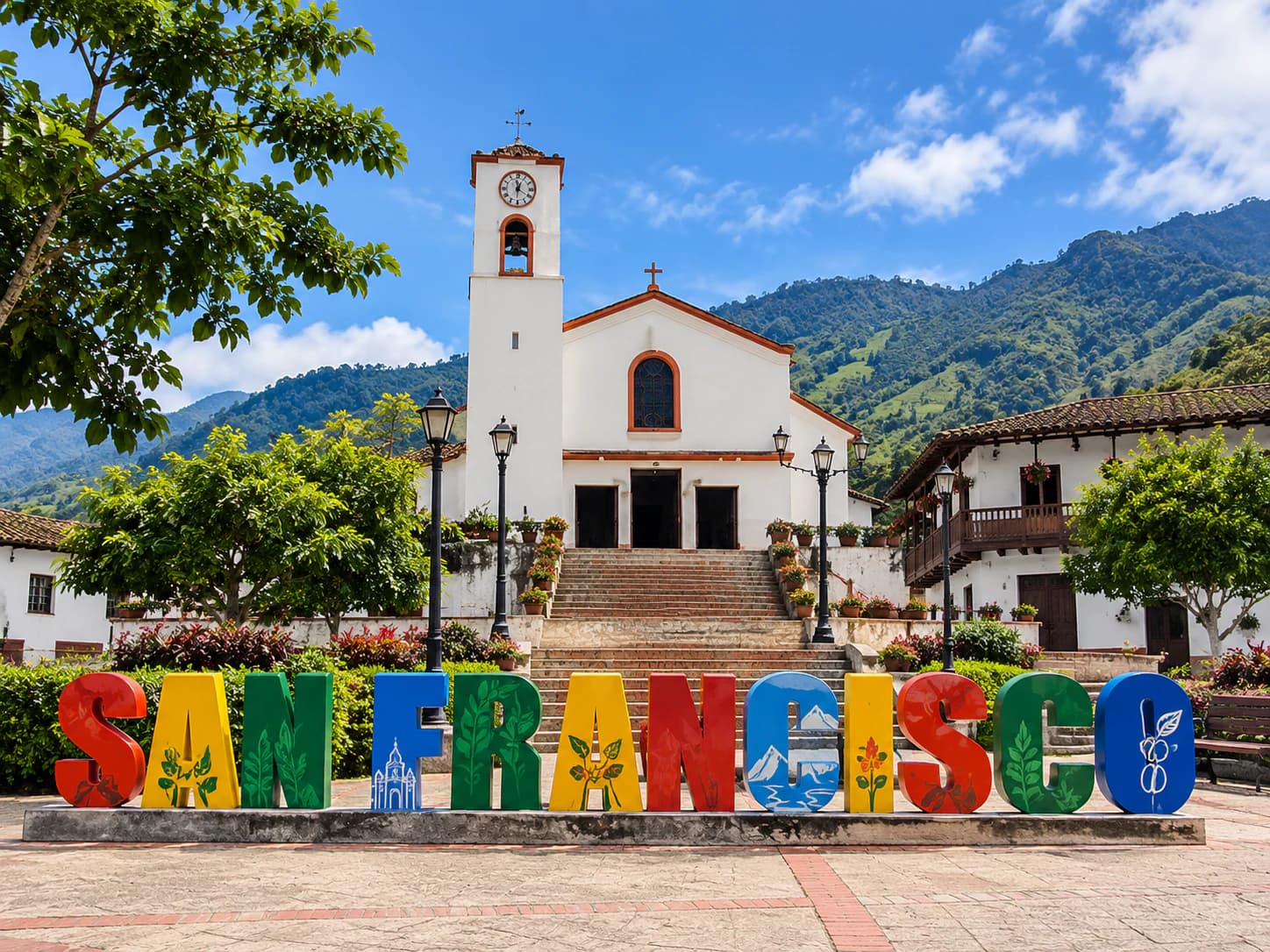 Iglesia blanca con reloj y letrero colorido que dice San Francisco, rodeada de montañas y árboles.