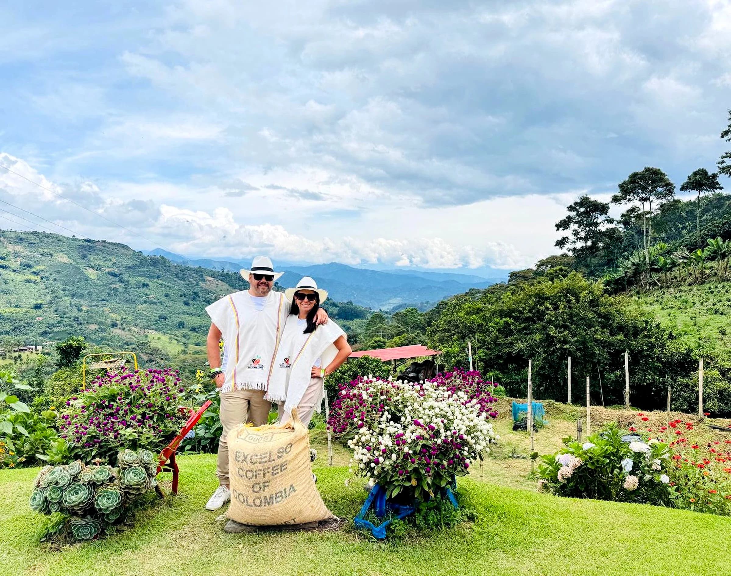 Pareja posando en un paisaje montañoso de Jardín, rodeados de flores y sacos de café.