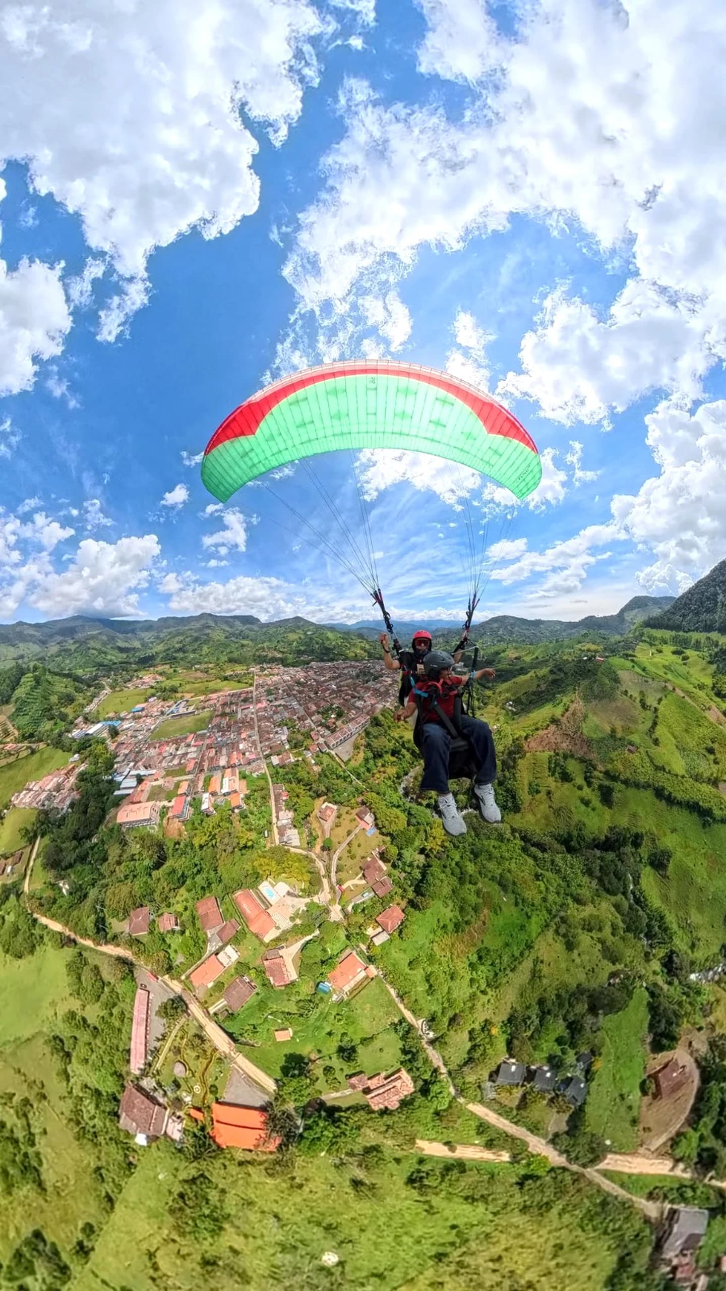 A paraglider soaring over the lush green mountains and town of Jardín, Antioquia.